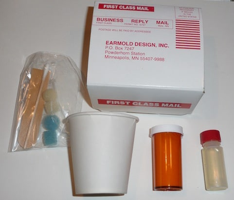Figure 4.  Acrylic ear impression kit.  This consisted of a powder (brown container), catalyst (clear bottle with red cap), a paper cup in which the ingredients are mixed, using a wooden spatula (in bag), otoblocks and Q-tip also in the bag, and a self-mailer container in which to send the impression to an earmold laboratory where the earmold will be made.